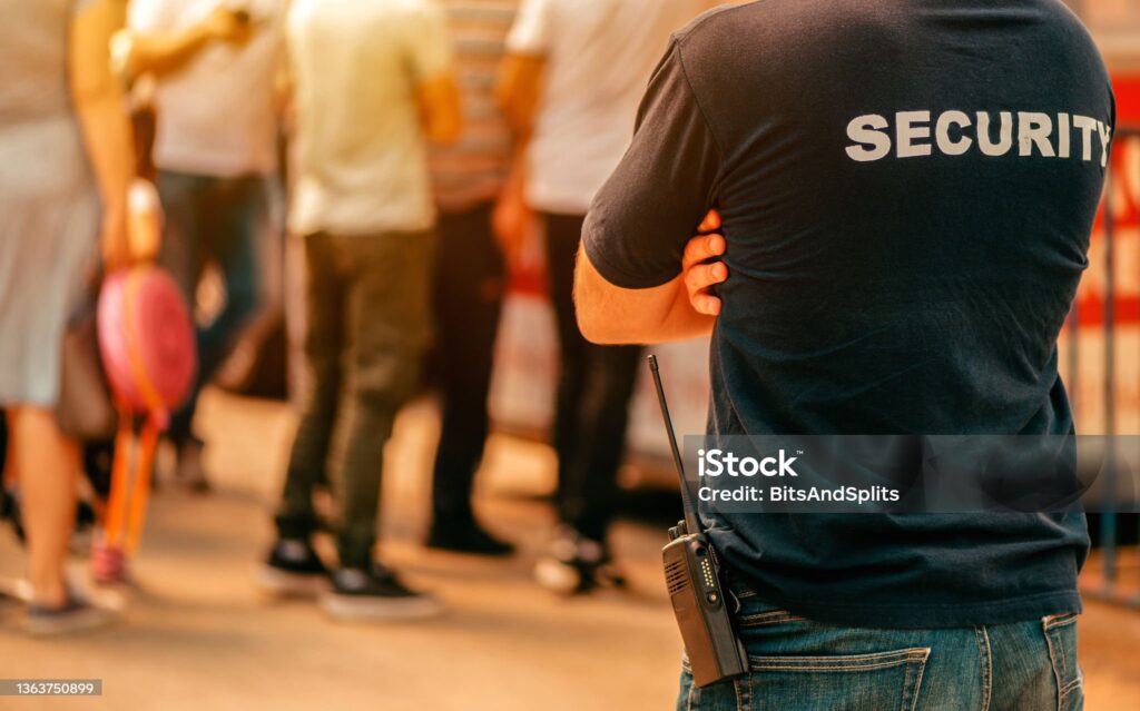 Mitarbeiter eines Sicherheitsdienstes neben einer friedlichen Menschenmenge an einem Eingangsbereich